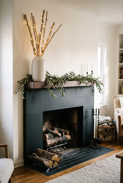 Modern black fireplace with a floating mantel, a tall vase of birch branches wrapped in tiny lights and a low olive garland
