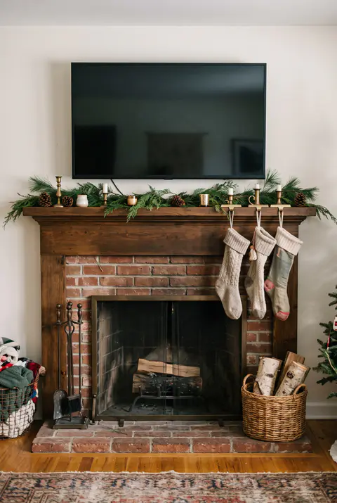 Fireplace with a TV mounted above, the mantel decorated with a slim garland kept below the screen, small candles and stockings