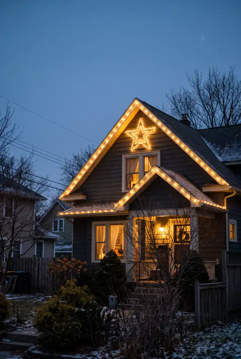 House at dusk with a large lighted star mounted high on the front gable and warm white lights along the roofline