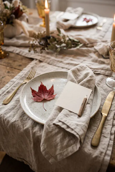 Thanksgiving place setting with a red maple leaf on the plate and a blank card and pencil tucked into the linen napkin
