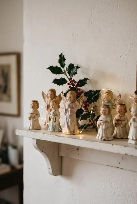 Vintage-style ceramic angel figurines and small choir singer candle holders on a white shelf with holly and warm lights