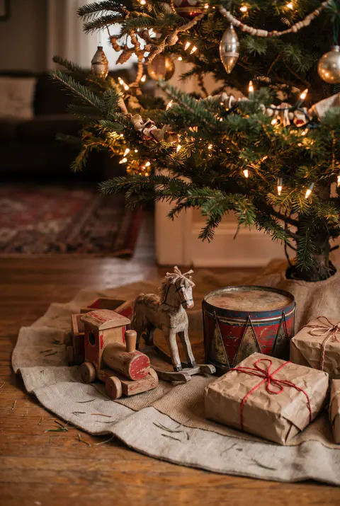 Vintage wooden toys under a Christmas tree, including a small wooden train, a tin drum, a rocking horse and gifts in brown paper