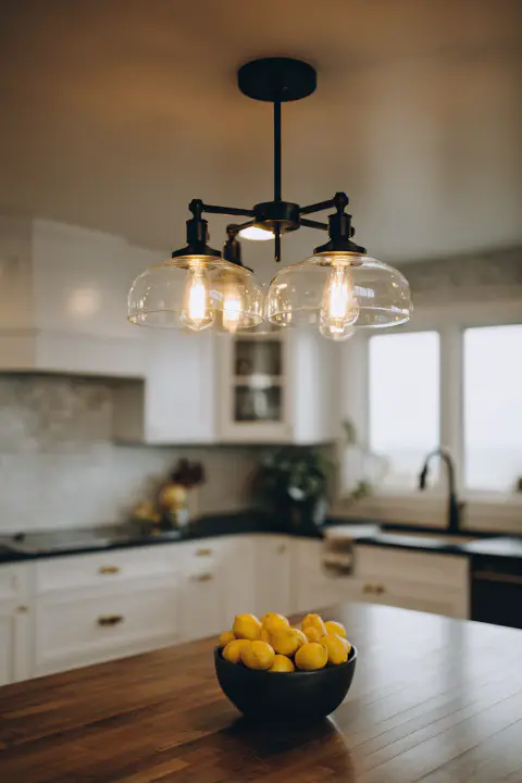 Farmhouse kitchen island with bowl of lemons. Modern farmhouse kitchen design with black chandelier, white cabinets, and wooden island top. Rustic kitchen decor a