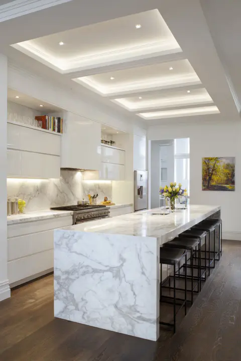 Luxurious white marble kitchen with a large waterfall island and recessed lighting, perfect for modern home design and elegant entertaining