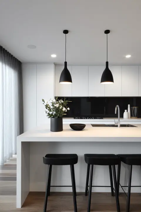 Modern minimalist kitchen interior design with white countertops, black pendant lights, a black backsplash, and sleek black bar stools. Features a white floral arrangement in a black vase, a stainless steel sink, and light wood flooring. Ideal for modern kitchen inspiration, minimalist home decor, and contemporary interior design ideas