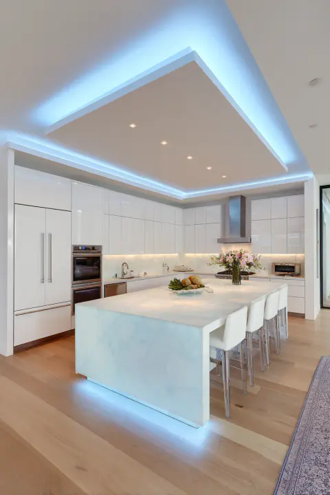 Modern white kitchen design with large marble island, blue LED lighting, stainless steel appliances, and hardwood floors. Ideal for contemporary home decor, luxury kitchens, and minimalist interior design inspiration. Kitchen island seating with white bar stools